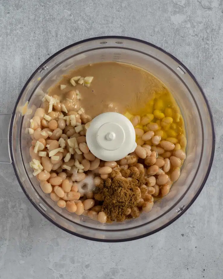 A food processor bowl filled with the ingredients needed to make white bean hummus, ready to be blended