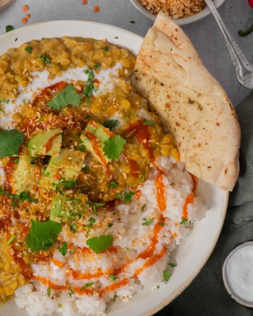 A hearty bowl of vegan red lentil dahl topped with creamy avocado, coriander and chilli sauce.
