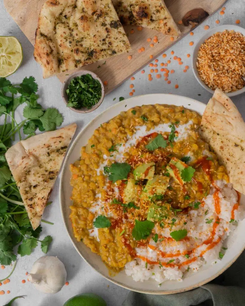 A hearty bowl of vegan red lentil dahl topped with creamy avocado, coriander and chilli sauce.