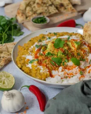 A hearty bowl of creamy vegan red lentil curry topped with avocado, coriander and chilli sauce.