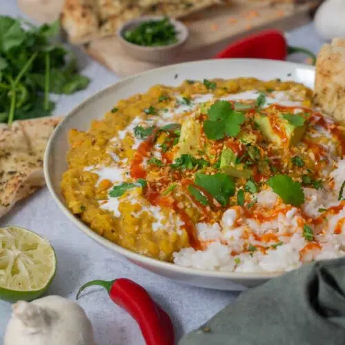 A hearty bowl of creamy vegan red lentil curry topped with avocado, coriander and chilli sauce.