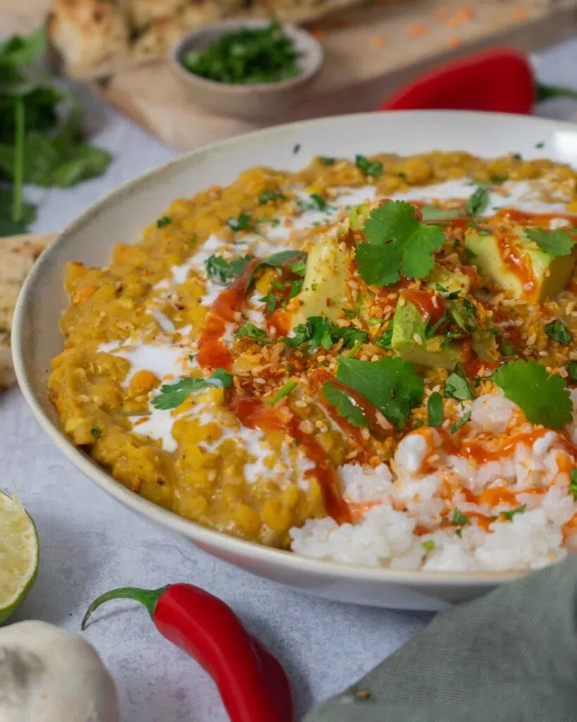 A hearty bowl of vegan red lentil dahl topped with creamy avocado, coriander and chilli sauce.