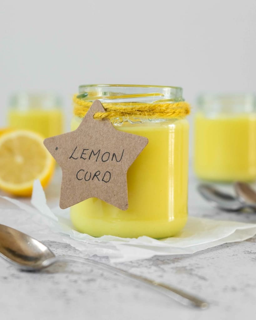 A jar of vibrant yellow vegan lemon curd with a cute cardboard star label tied on with yellow string