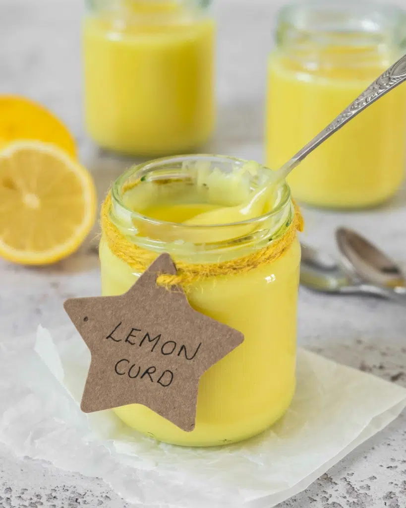 A jar of vibrant yellow vegan lemon curd with a cute cardboard star label and a vintage spoon resting in the jar