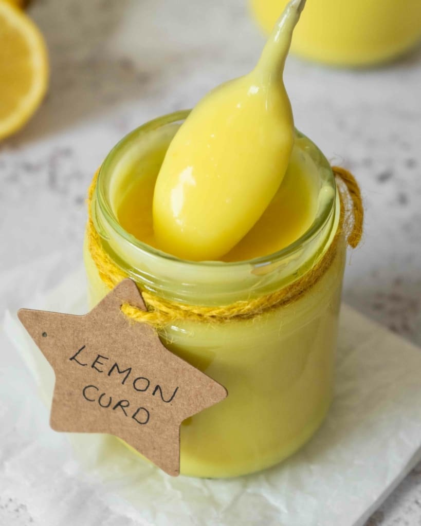 A jar of vibrant yellow vegan lemon curd with a spoonful being slowly removed