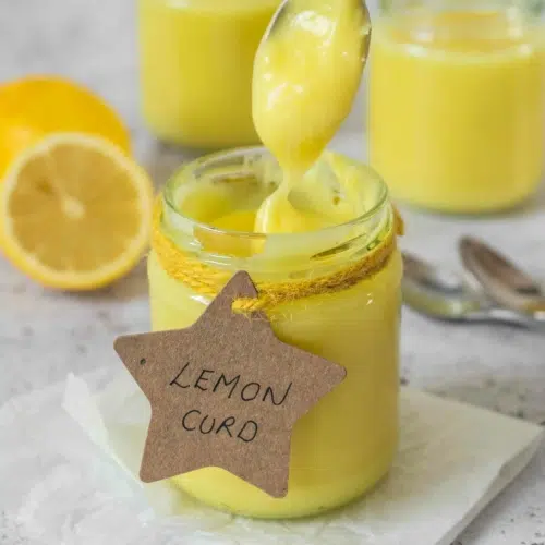 A jar of vibrant yellow vegan lemon curd with a spoonful being slowly removed