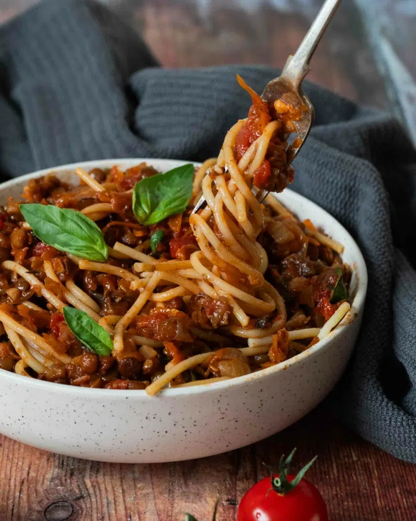 A bowl of vegan bolognese with a forkful of spaghetti being twirled out of it and lifted up.