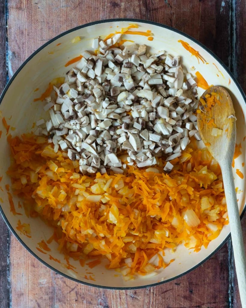 Cooked carrots and onions in pan alongside diced fresh white mushrooms, ready to be fried