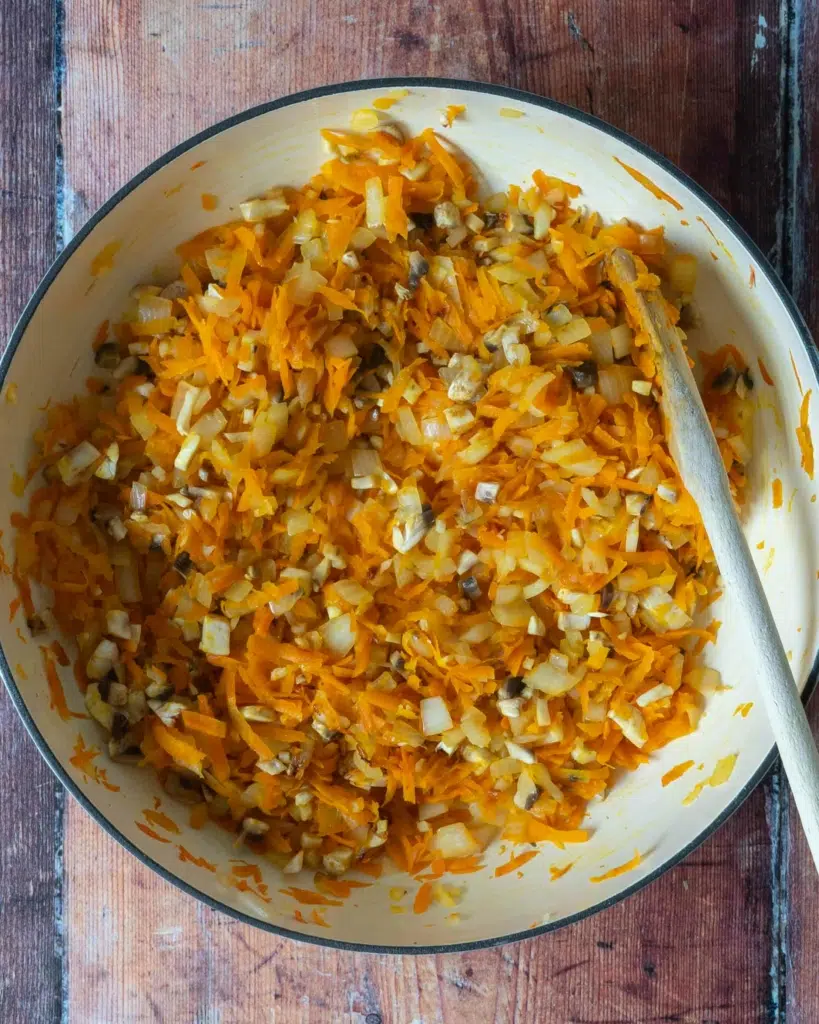 Grated carrot, diced onion, minced garlic and diced mushrooms in a pan having been fried until softened