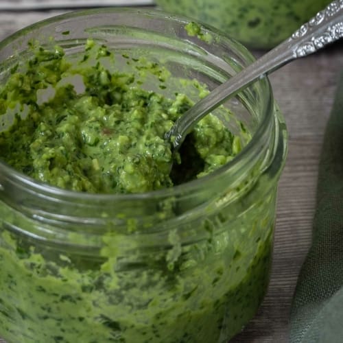 A close up photo of a glass jar containing fresh, vibrant green basil pesto.