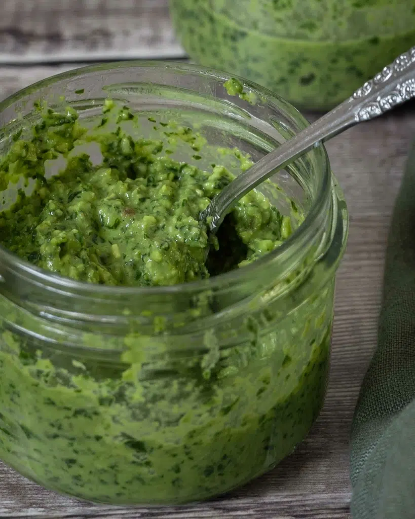 A close up photo of a glass jar containing fresh, vibrant green basil pesto.
