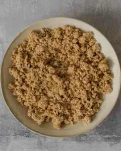 Instructions on how to make oatmeal crumble topping. This process shot shows the crumble topping in a bowl after the butter has been rubbed into the oat flour and sugar.