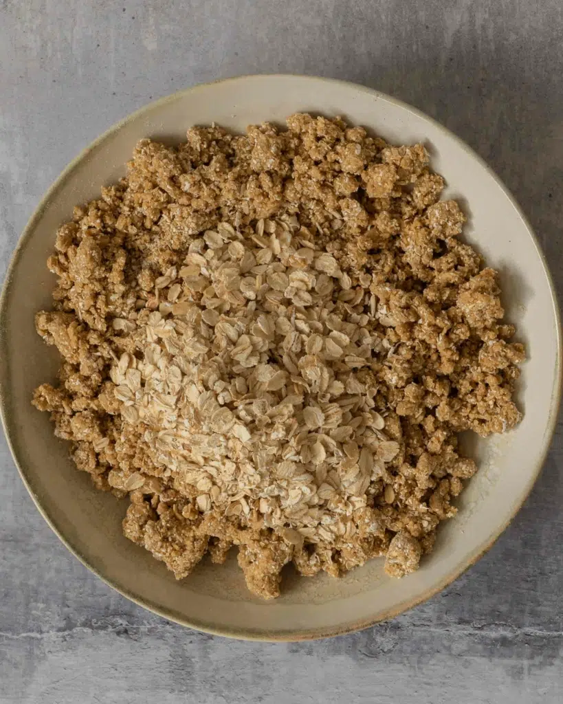 Oatmeal crumble topping in a bowl with some whole oats sprinkled on top, ready to be stirred in.