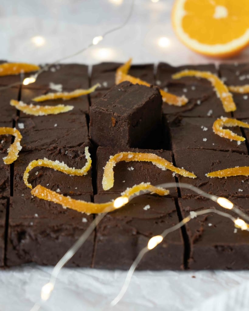 A side on photo of some festive chocolate orange fudge, with fairy lights and fresh orange