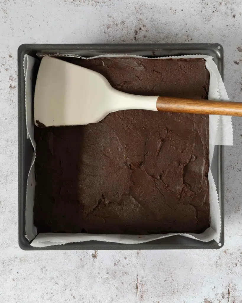 A lined baking tin with 5 ingredient chocolate orange fudge pressed into it, ready to be refrigerated
