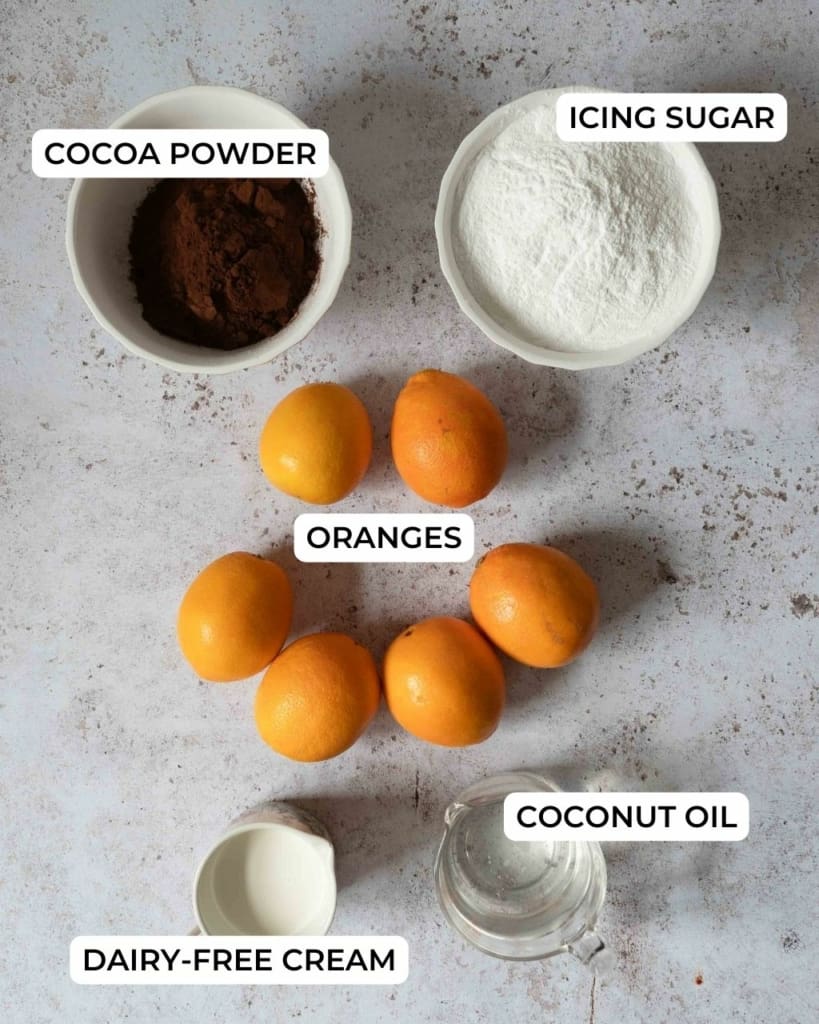 Cocoa powder, icing sugar, oranges, coconut oil and dairy free cream on a table top, ready to make 5 ingredient fudge