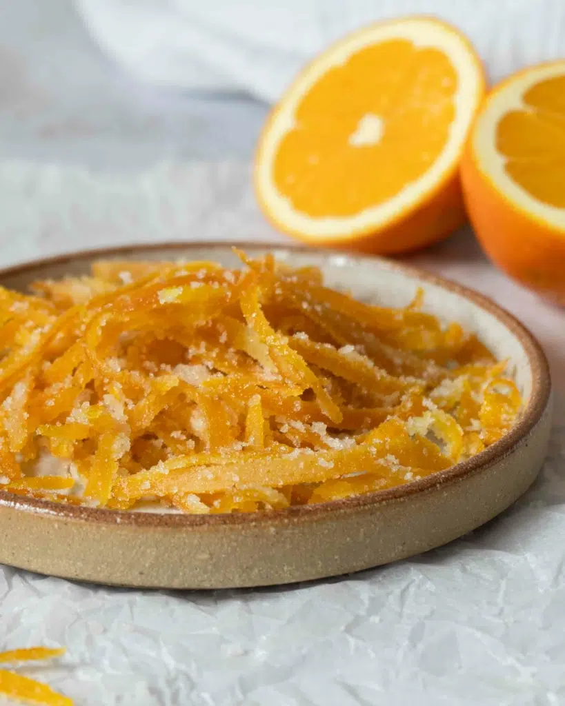 A side on photograph of a plate of vibrant candied orange peel