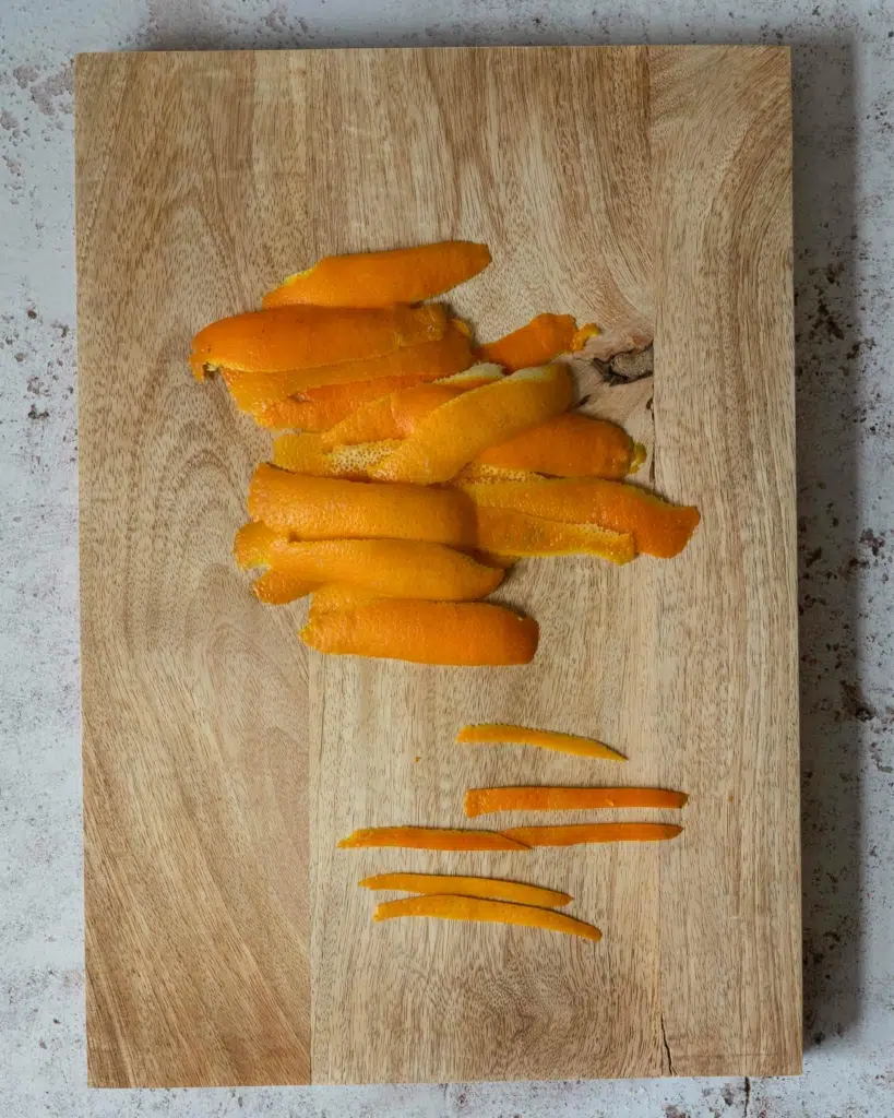 A chopping board with thick and thin slices of fresh orange peel