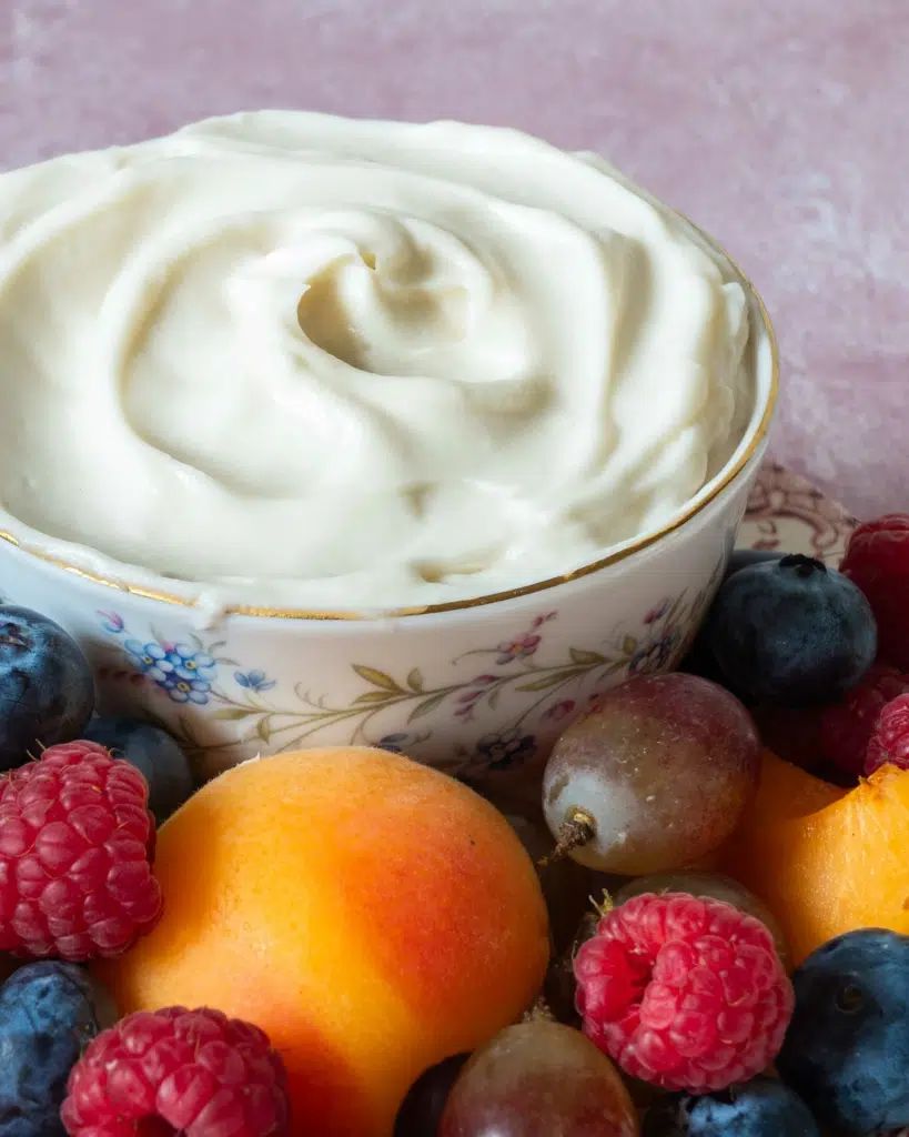 A close up photograph to accompany a vegan fruit dip recipe, showing a plate of colourful fruit and a vintage bowl filled with whipped vegan fruit dip