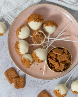 White chocolate Biscoff cake pops laid on a peach coloured plate, dusted with Biscoff biscuit crumbs