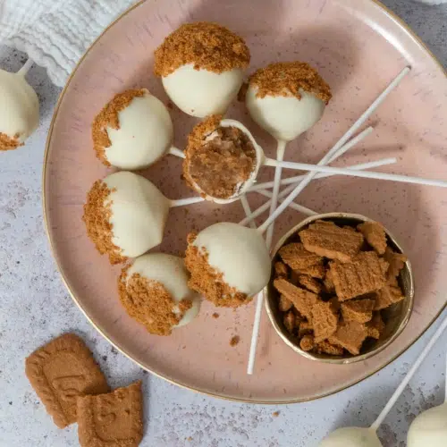 White chocolate Biscoff cake pops laid on a peach coloured plate, dusted with Biscoff biscuit crumbs