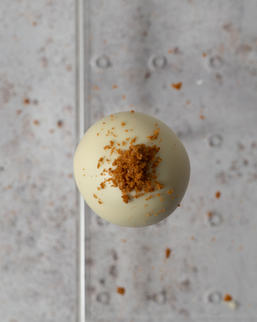 A birds eye view of a white chocolate Biscoff cake pop, showing the cake crumb decoration on top