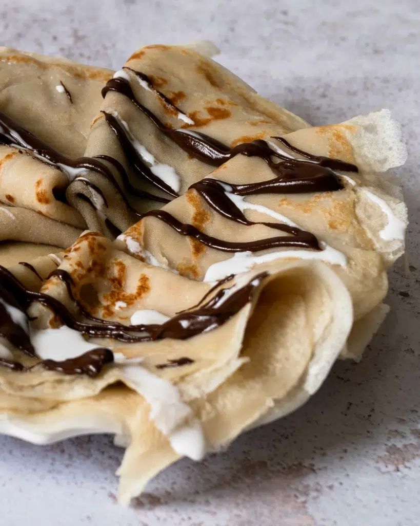 A plate of coconut milk crepes folded and drizzled with chocolate sauce and coconut cream
