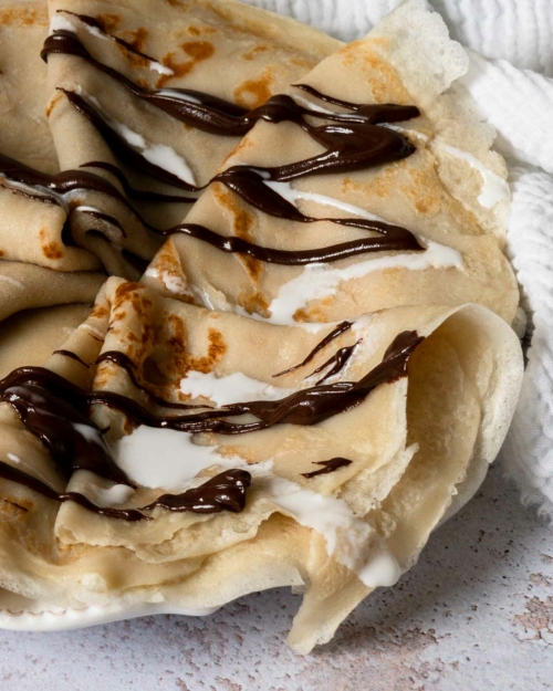 A close up of a plate of coconut milk crepes, drizzled in chocolate and cream