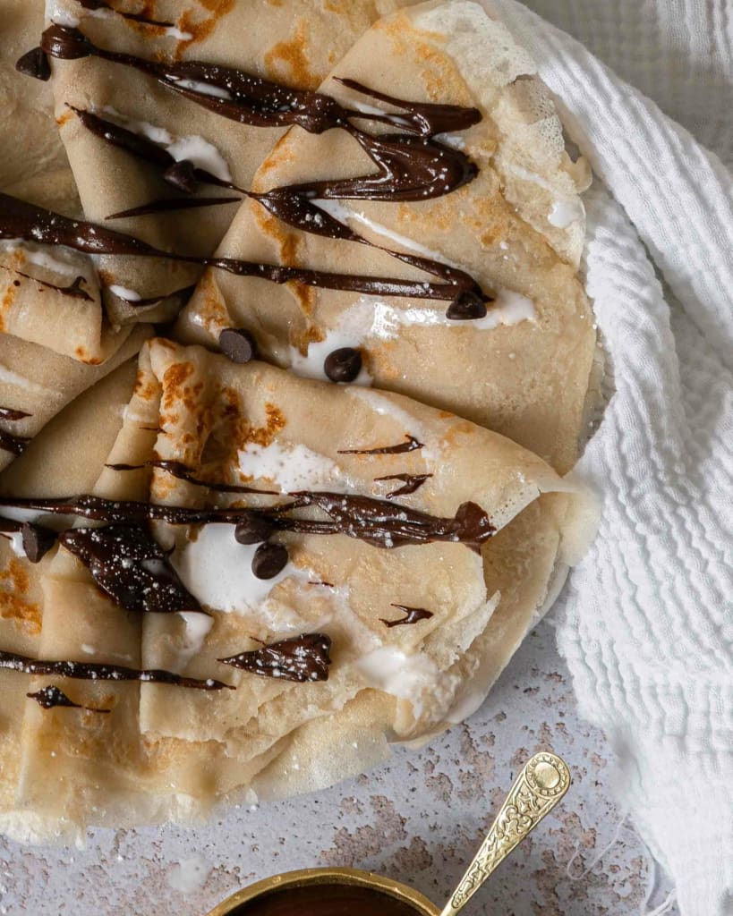 An overhead shot showing a plate of folded coconut milk crepes, drizzled in chocolate ganache and dairy free cream