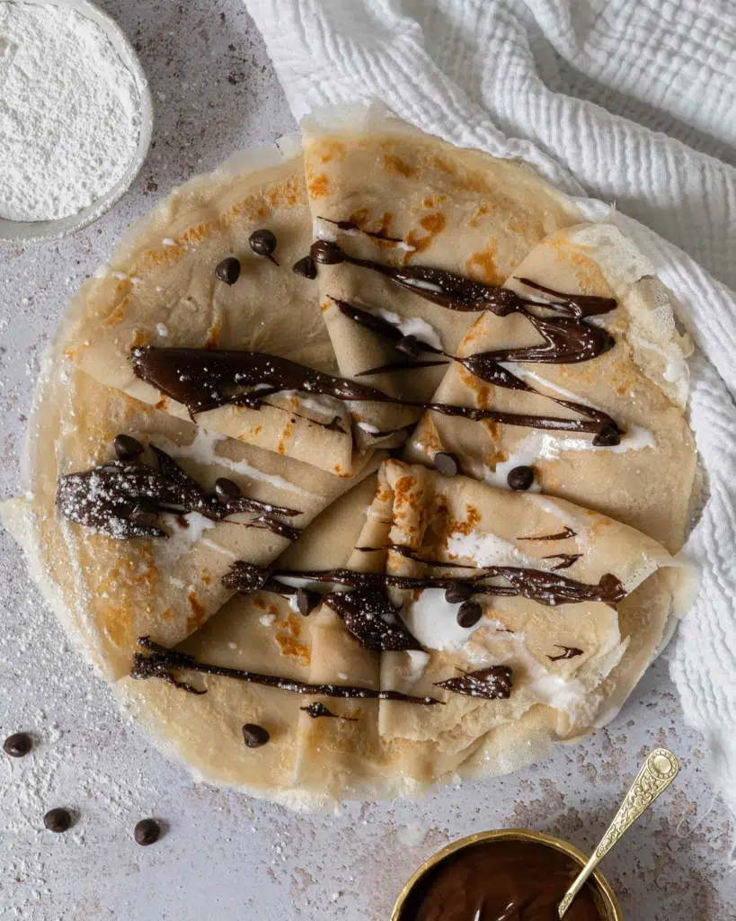 An overhead photo of a plate of vegan coconut milk crepes drizzled in dairy free chocolate and cream and sprinkled with chocolate chips