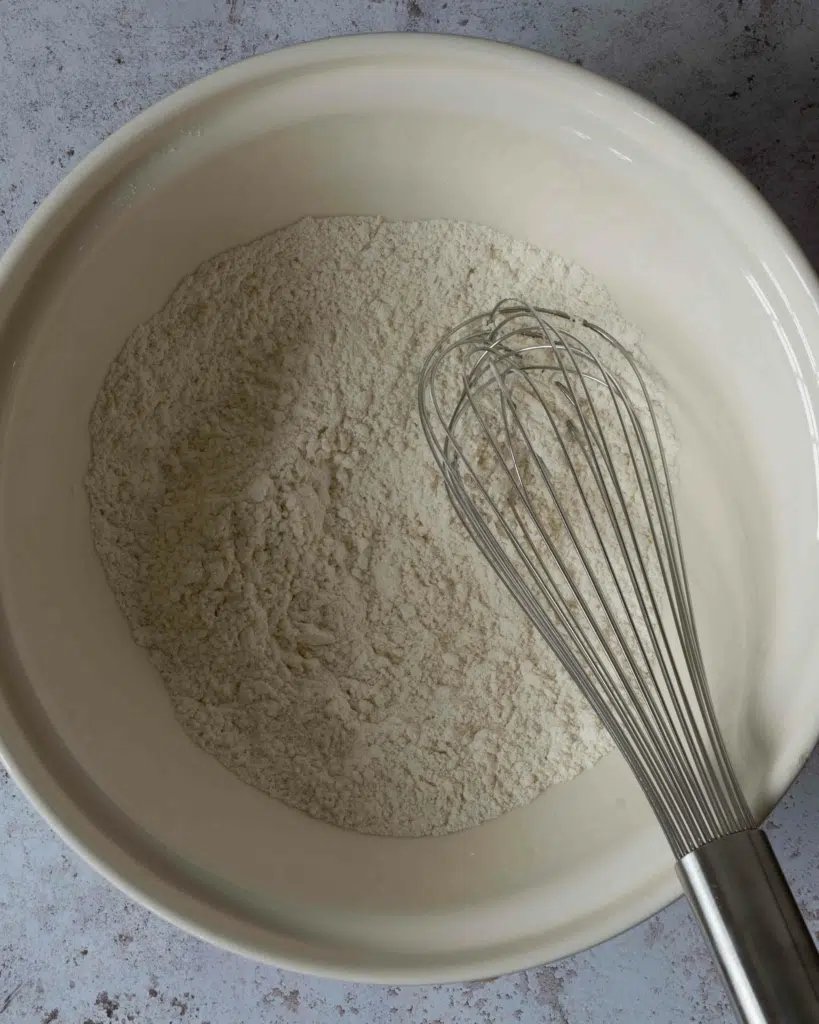 A bowl with a flour mixture in it and a metal whisk sat on top