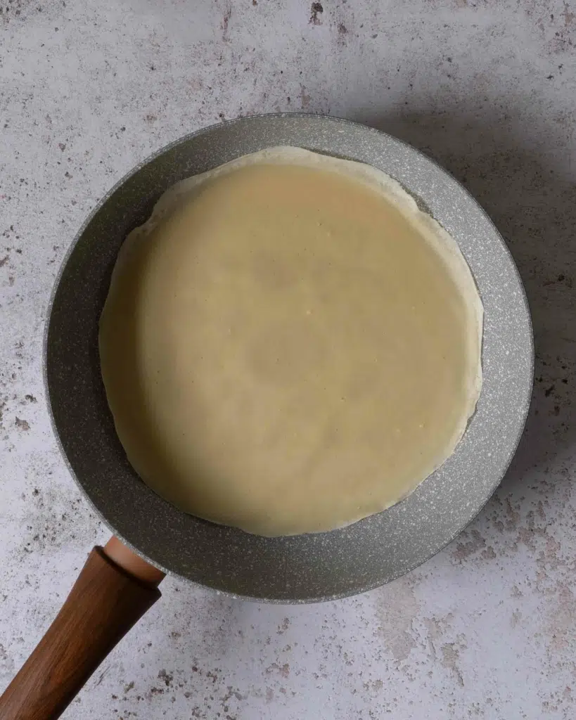 A frying pan with a partially cooked crepe in it