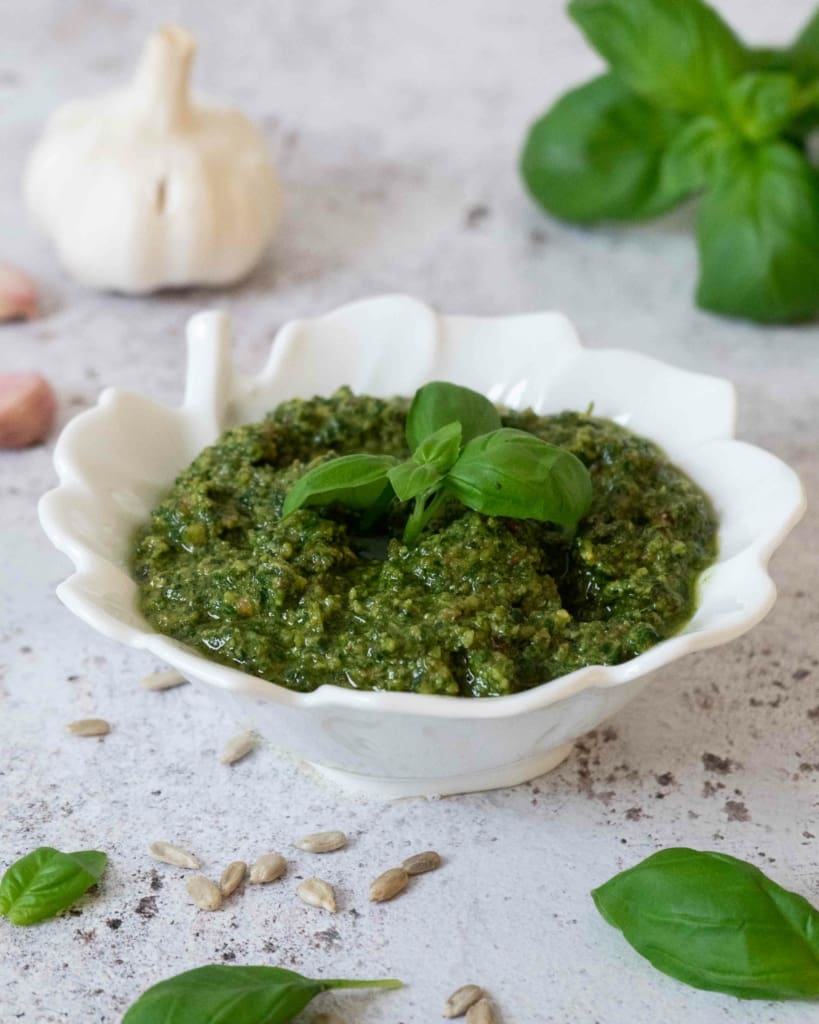 A bowl of fresh, green vegan pesto without pine nuts. Topped with fresh basil leaves.