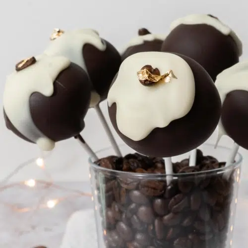 Tiramisu cake pops sat in a glass cup filled with coffee beans