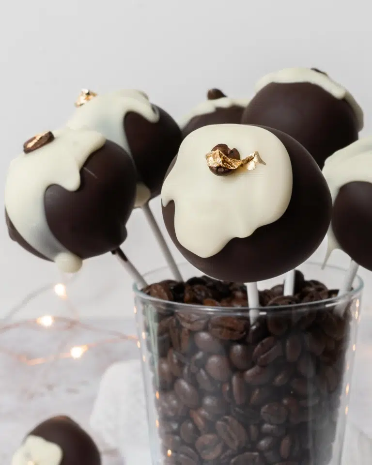 Tiramisu cake pops sat in a glass cup filled with coffee beans