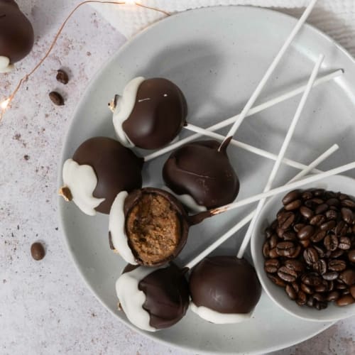 An overhead photo of a plate scattered with tiramisu cake pops, one with a bite taken out of it