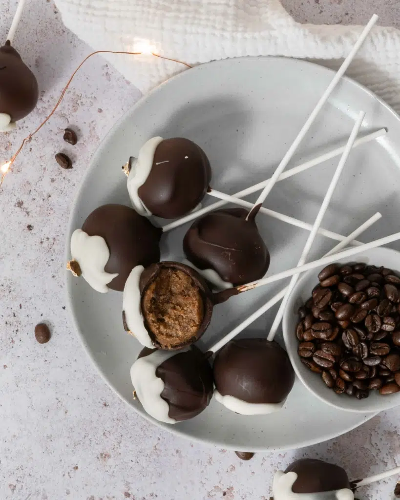 An overhead photo of a plate scattered with tiramisu cake pops, one with a bite taken out of it