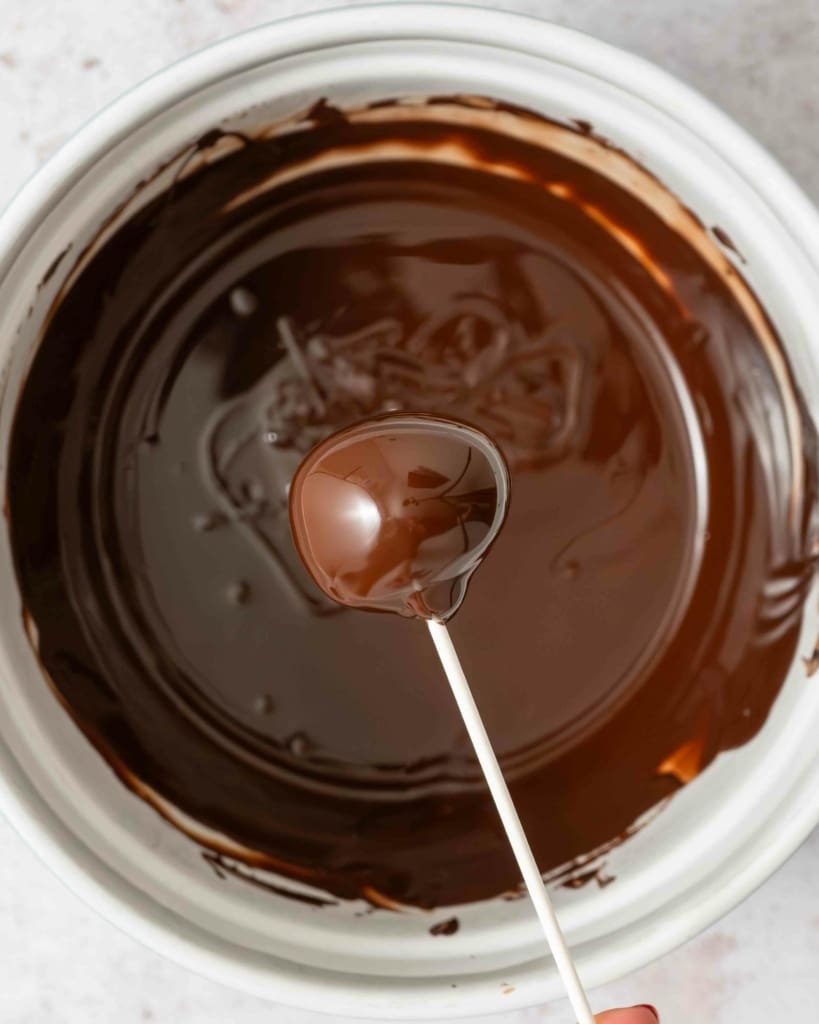 Holding a chocolate coated cake pop over a bowl of melted chocolate
