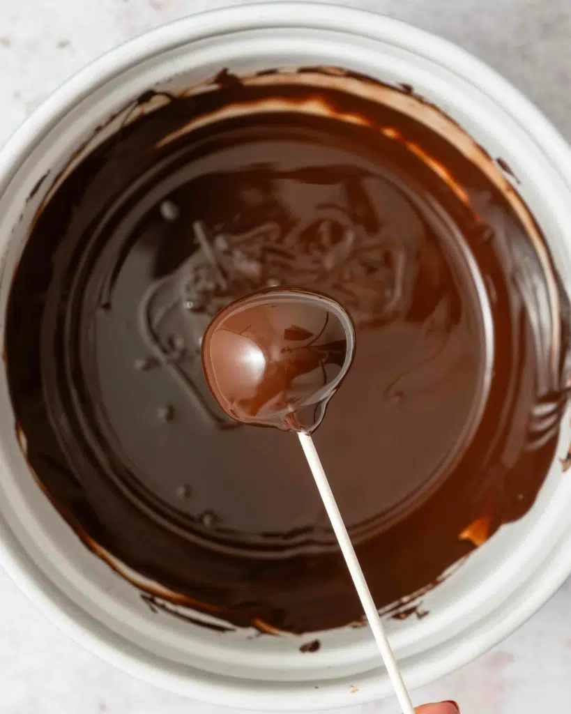 Holding a chocolate coated cake pop over a bowl of melted chocolate