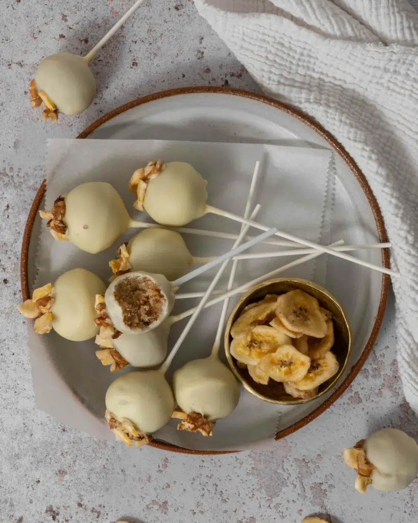 A plate of white chocolate banana bread cake pops topped with banana chips and walnuts