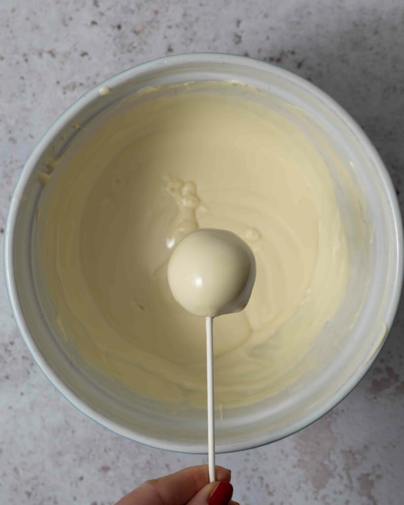 A cake pop being covered in white chocolate