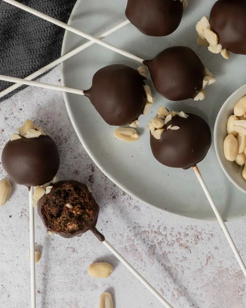Chocolate covered cake pops laying on a plate, topped with chopped peanuts