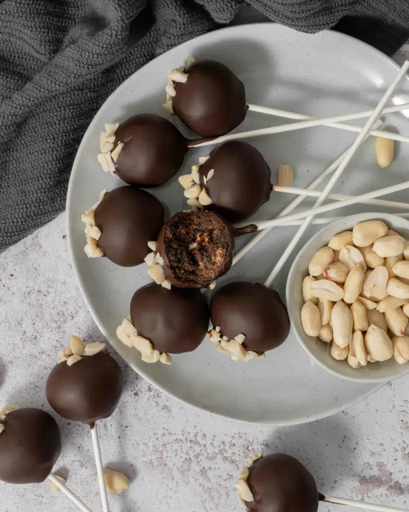A plate full of dark chocolate peanut butter cake pops, one with a bite taken out of it
