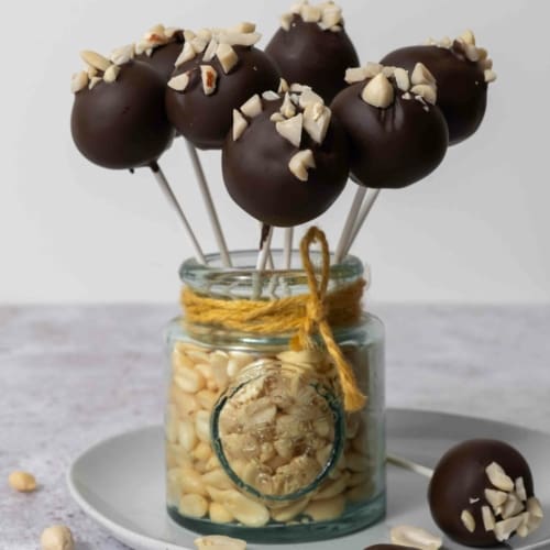A jar of peanuts holding up chocolate peanut butter cake pops, topped with chopped peanuts
