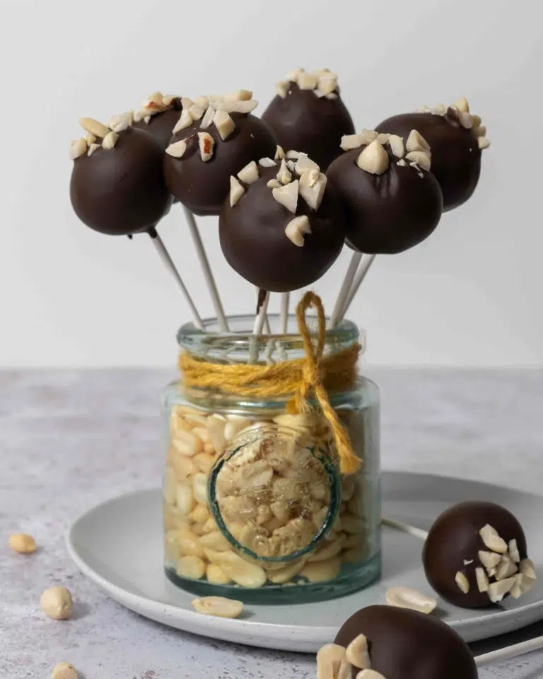 A jar of peanuts holding up chocolate peanut butter cake pops, topped with chopped peanuts