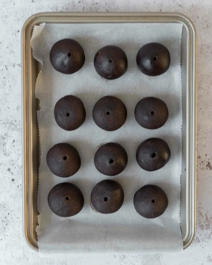 Chocolate peanut butter cake pops rolled out, with holes pressed into their centres and placed on a lined tray