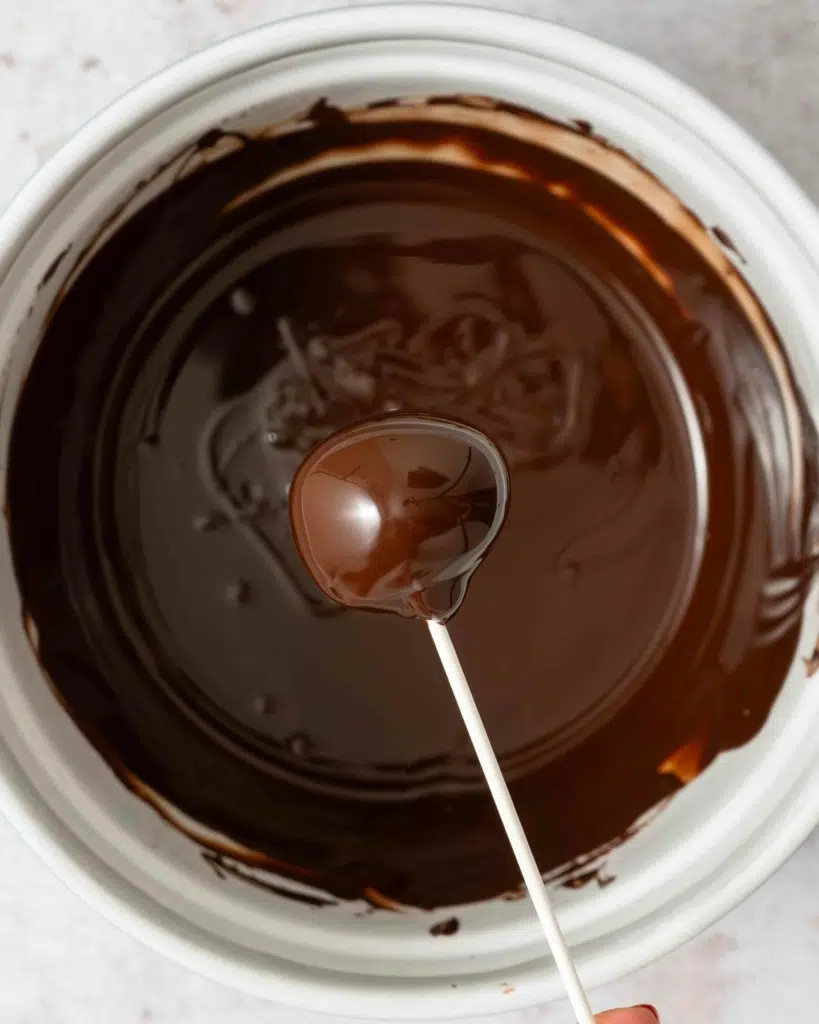 A cake pop being covered in melted dark chocolate