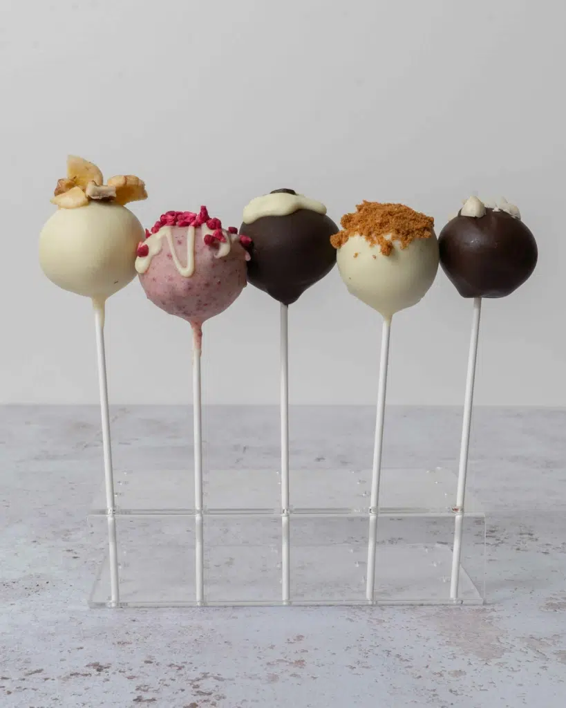 Five pretty cake pops in a stand with different toppings and flavours. Mothers day cake pop ideas!