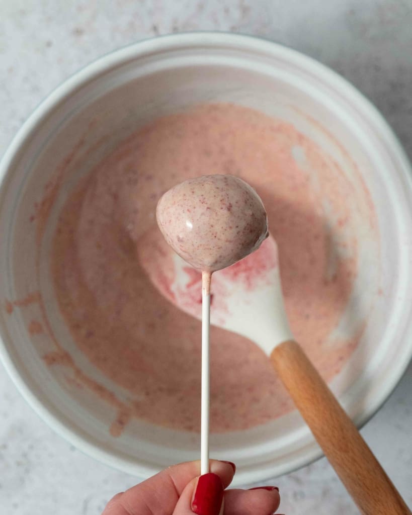A bowl of speckled pink raspberry white chocolate and one chocolate coated cake pop