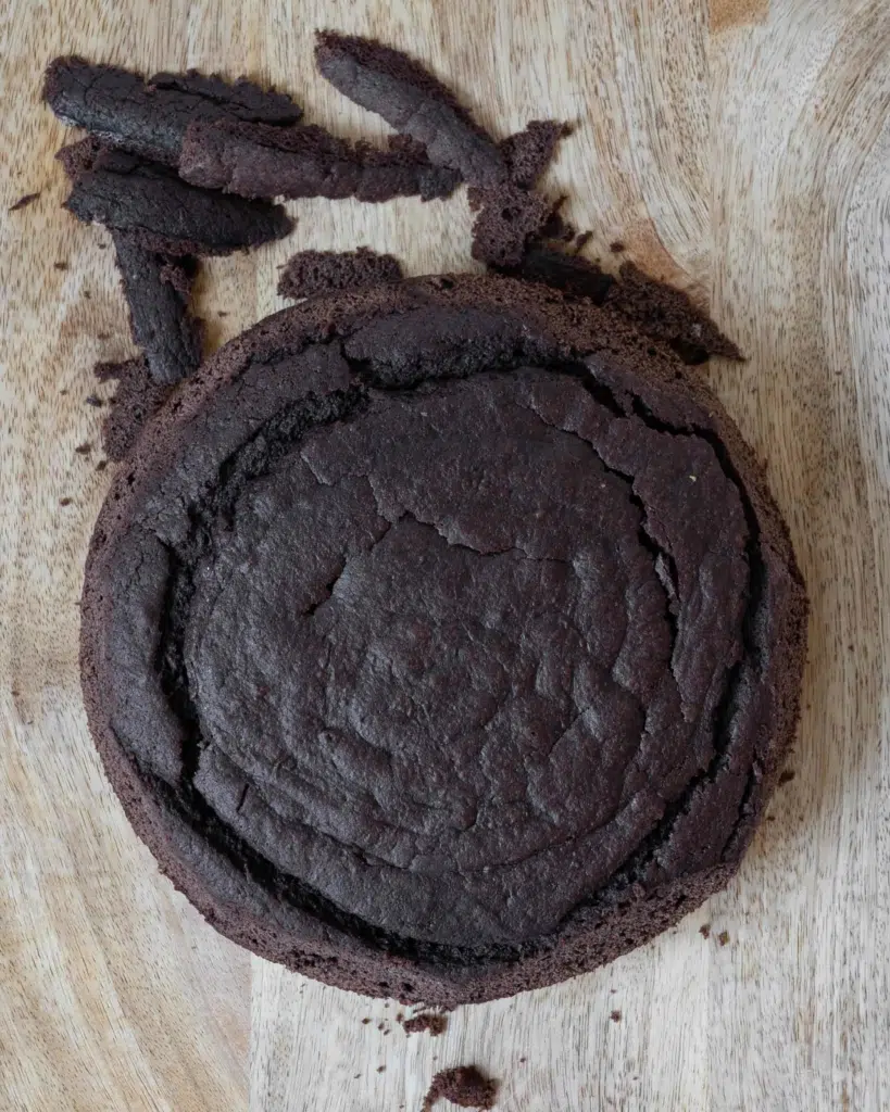A chocolate cake being trimmed on a chopping board.